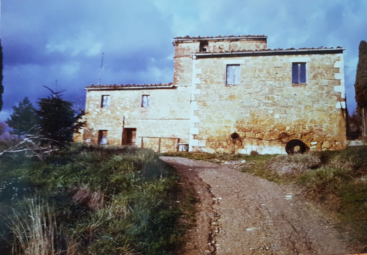 The farmhouse before its restoration: bare stone walls and the white road climbing up to it