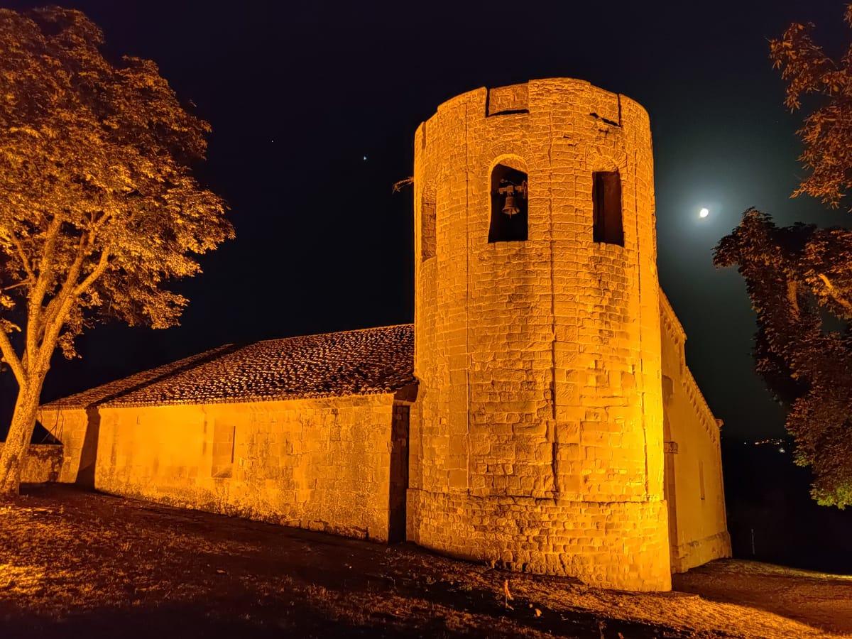 The cylindrical bell tower of the Pieve di Corsignano lit at night, with the moon
